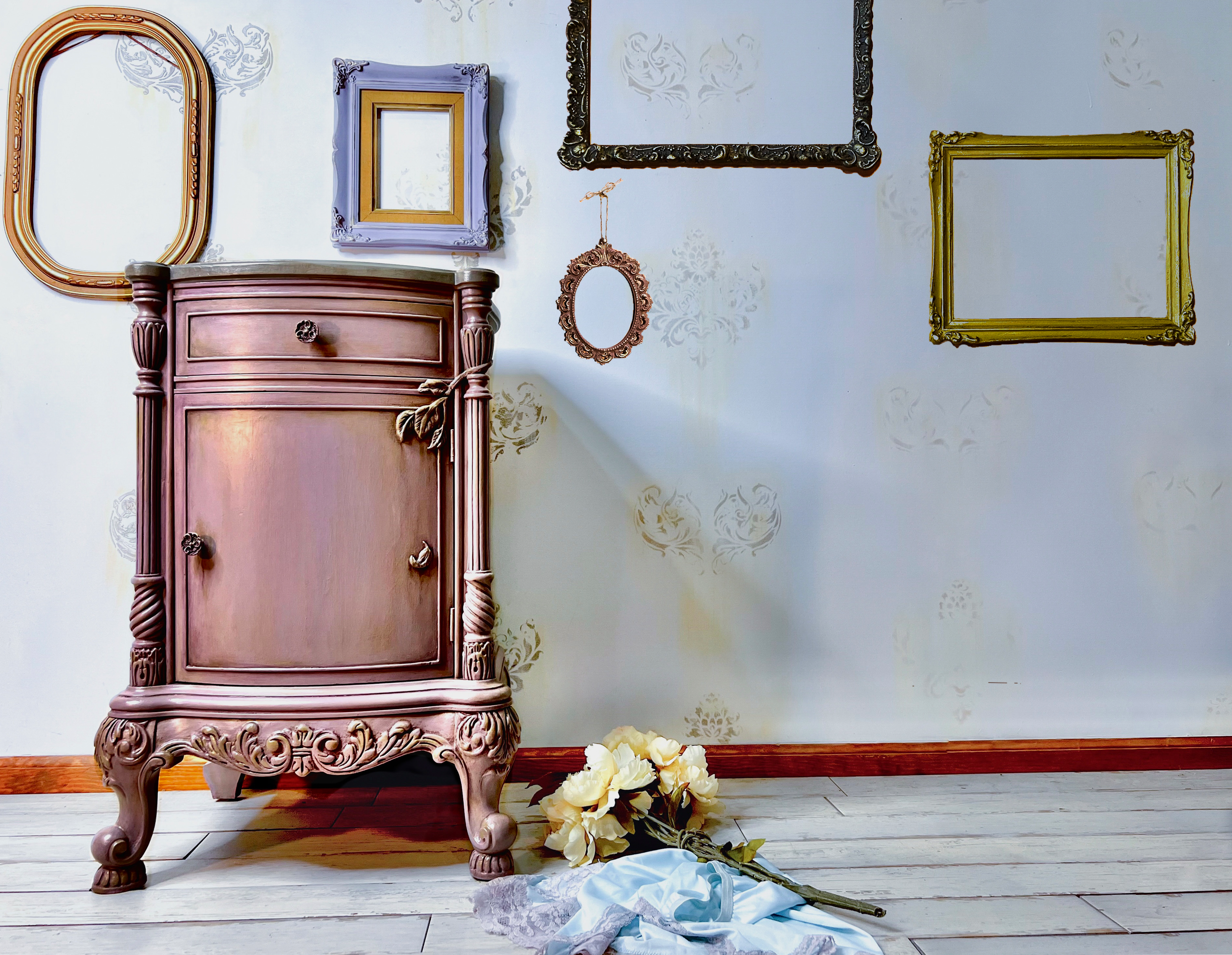 Painted Furniture with ornate carvings  in a room with vintage empty frames on the wall.